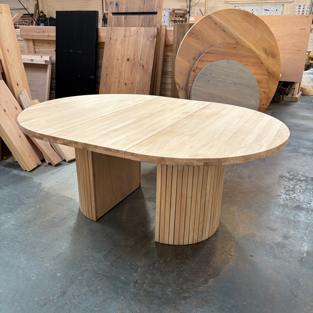 Round extending wooden table with chairs and a vase of flowers in a room.