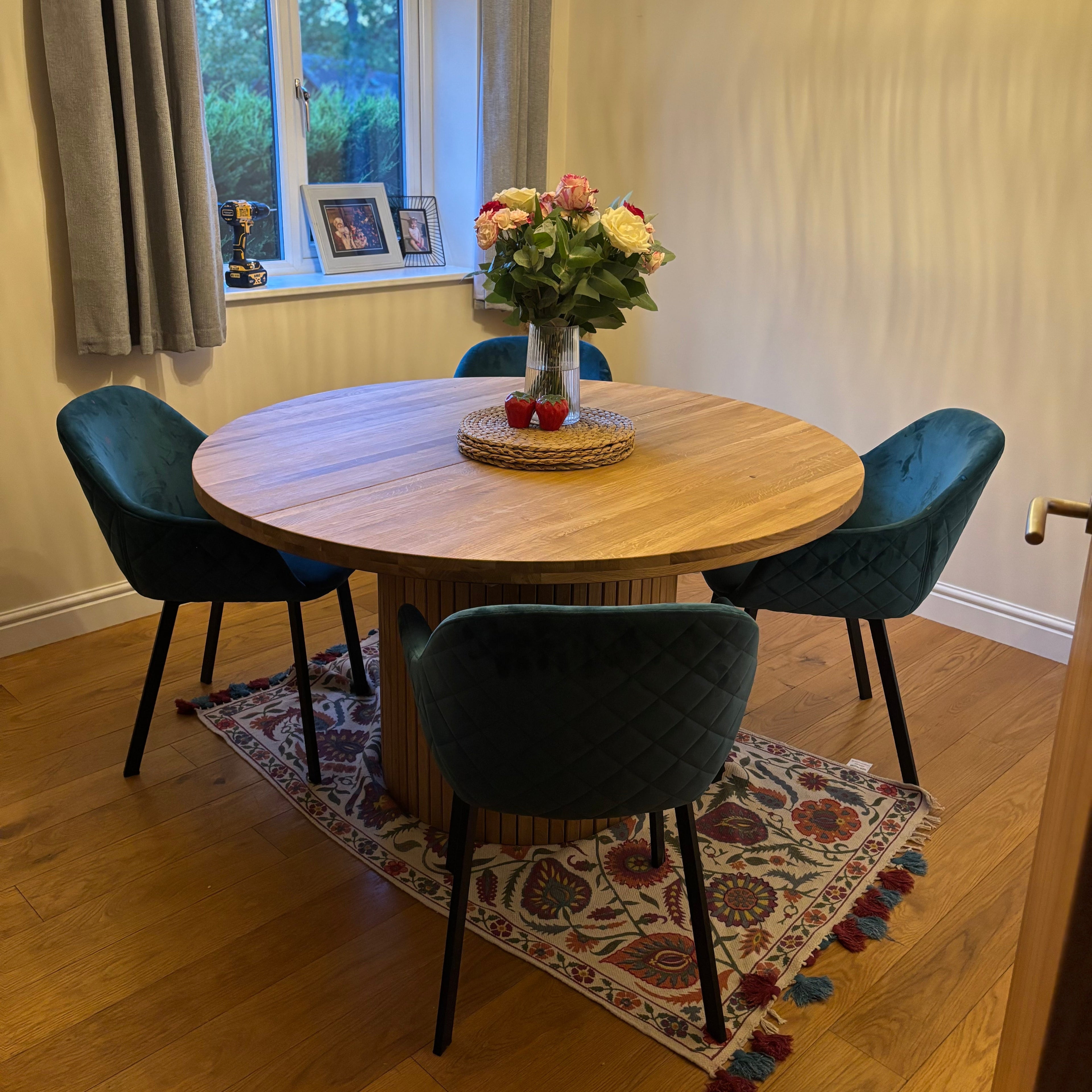 Dining room with a round EXTENDABLE wooden table and blue chairs, featuring a vase of flowers.
