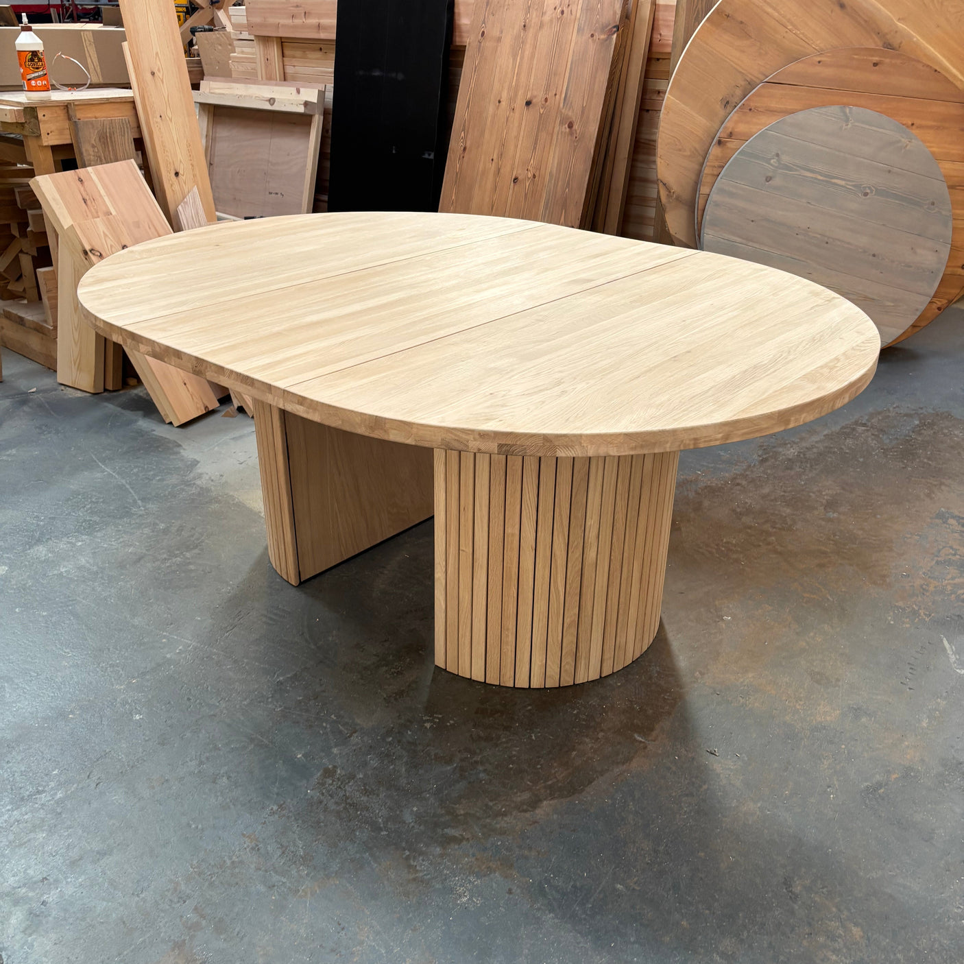 Round extending wooden table with chairs and a vase of flowers in a room.