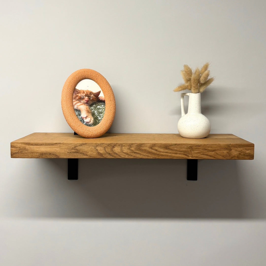 Wooden shelf with a round mirror and a vase on a plain wall.