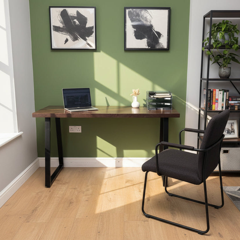 Wooden desk with laptop, printer, and small plant against a green wall.