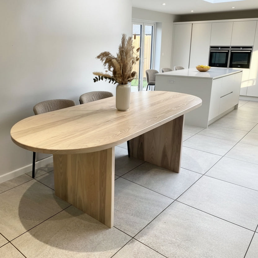 Wooden dining table in a modern kitchen setting with white cabinets and tiled floor.