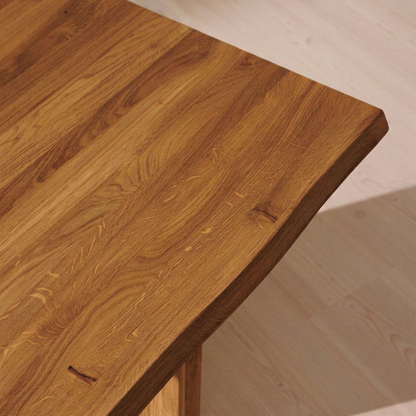 Close-up of a dark brown wooden table with a live edge and visible wood grain, set on a light wood floor.