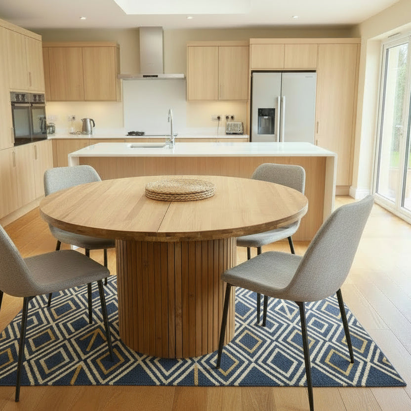 Round extending wooden table with chairs and a vase of flowers in a room.