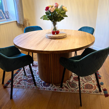 Round extending wooden table with chairs and a vase of flowers in a room.