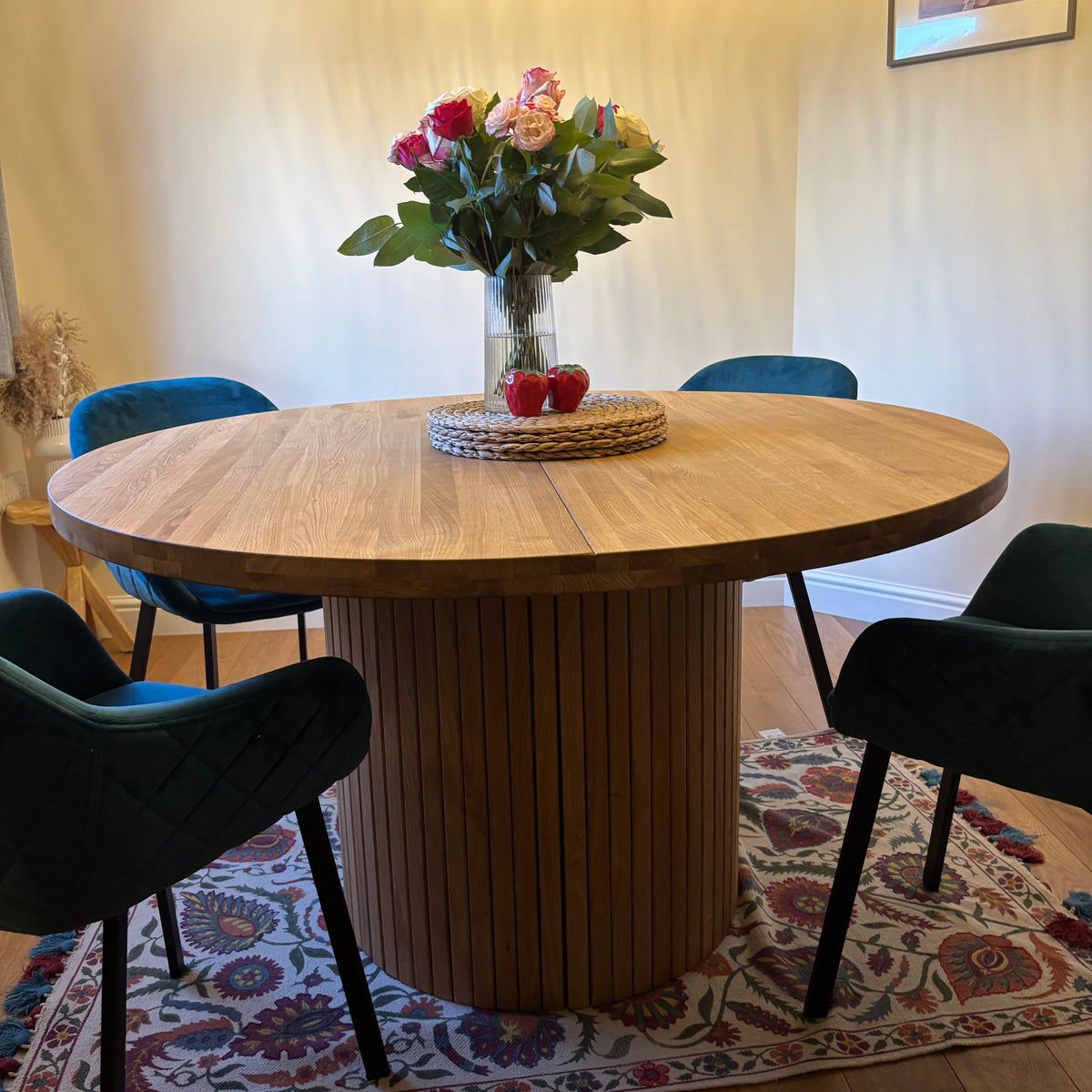 Round extending wooden table with chairs and a vase of flowers in a room.
