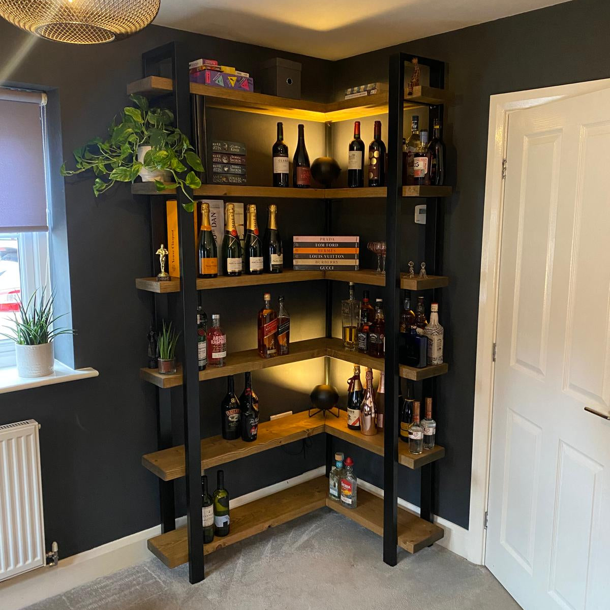 Wooden bookshelf with bottles against a dark wall in a room with a white door and radiator.
