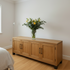 Wooden sideboard with a vase of flowers in a room with a bed and lamp.