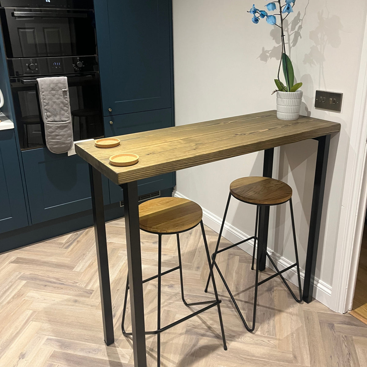 Wooden dining table with stools in a room with a blue floor and white walls.